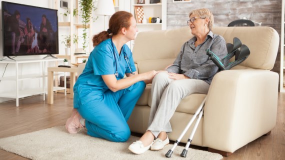 An image of a nurse talking to an elderly person on a cream sofa.